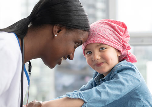 Female doctor speaking with young female patient. Patient wears a pink bandana.